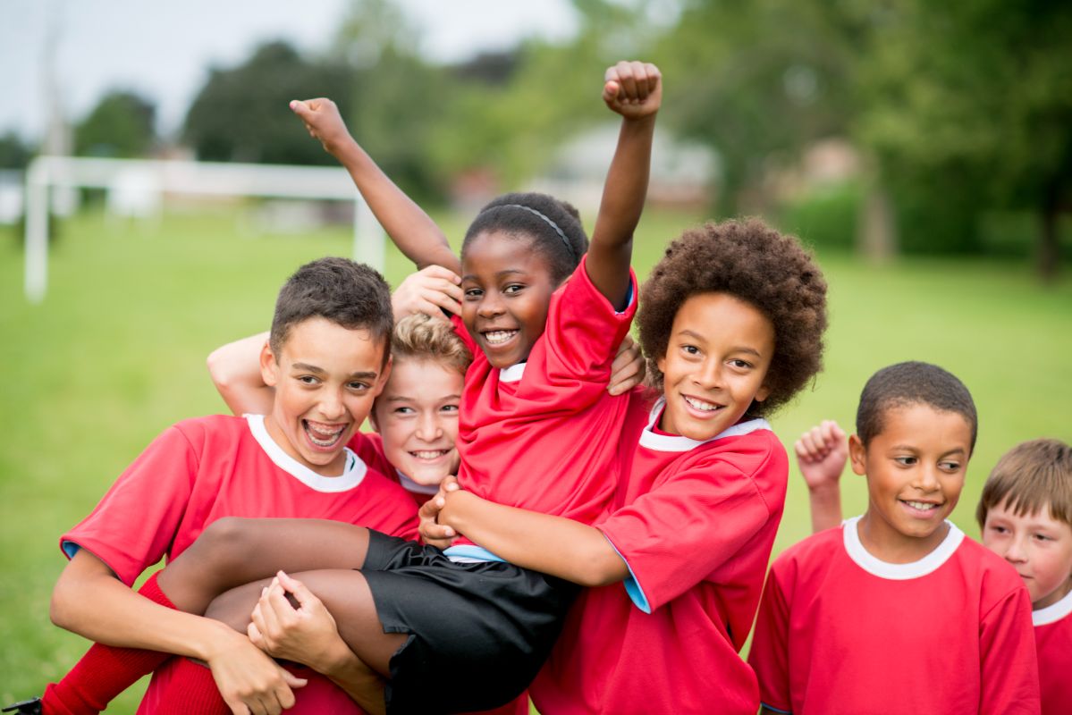 Group of children in red soccer jerseys celebrating, emphasizing teamwork and sports safety, relevant to pediatric dentistry and orthodontics at Coppe + Sears.