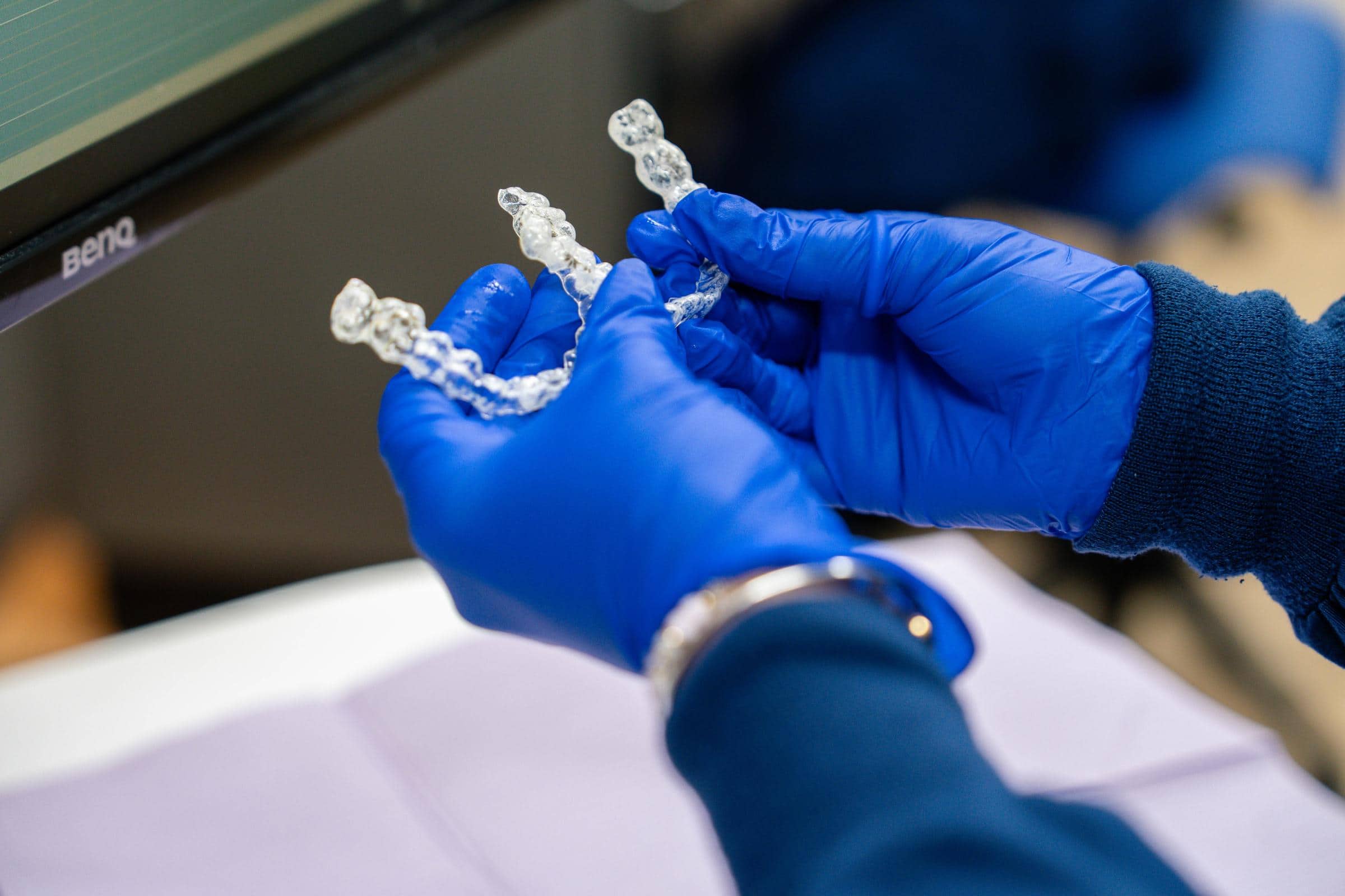 Hands wearing blue gloves holding clear aligners for orthodontic treatment at Coppe & Sears Orthodontics in Lexington, MA, emphasizing adult orthodontics and aesthetic improvement.