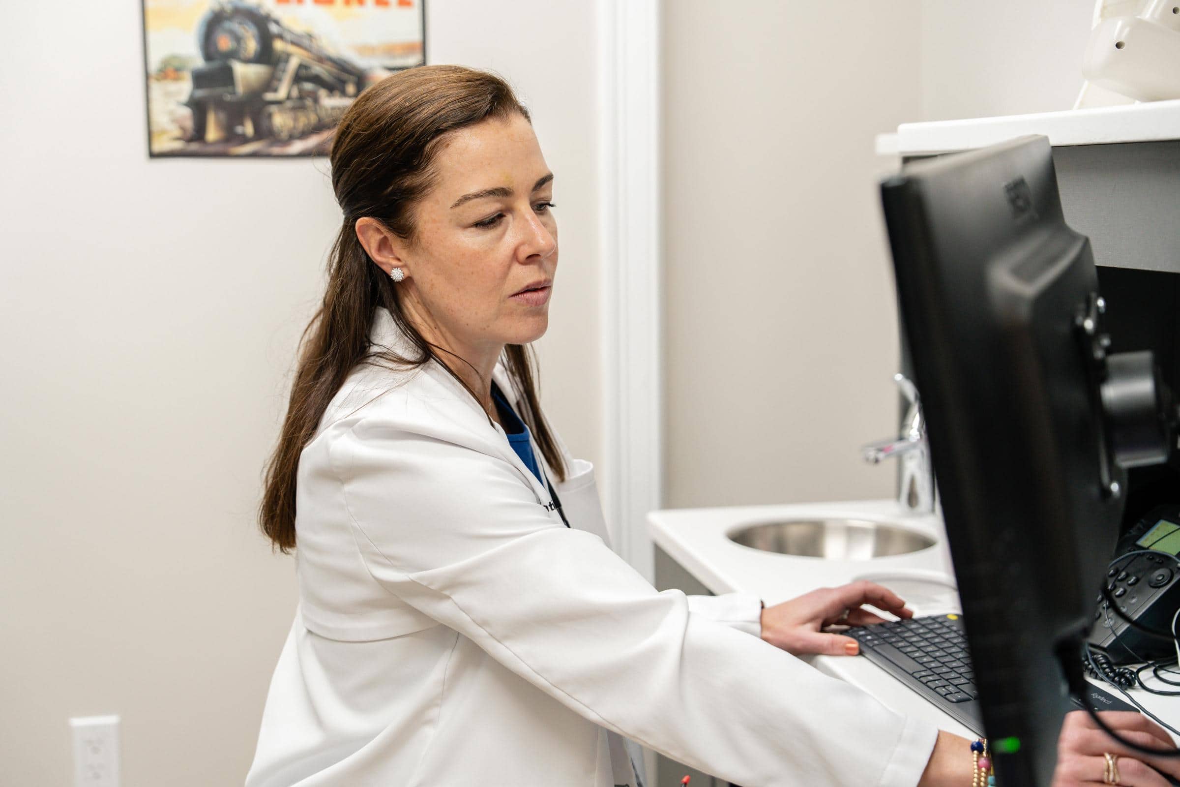 Pediatric dentist in white coat working on a computer in a dental office, representing Coppe + Sears Pediatric Dentistry and Orthodontics in Lexington, MA.