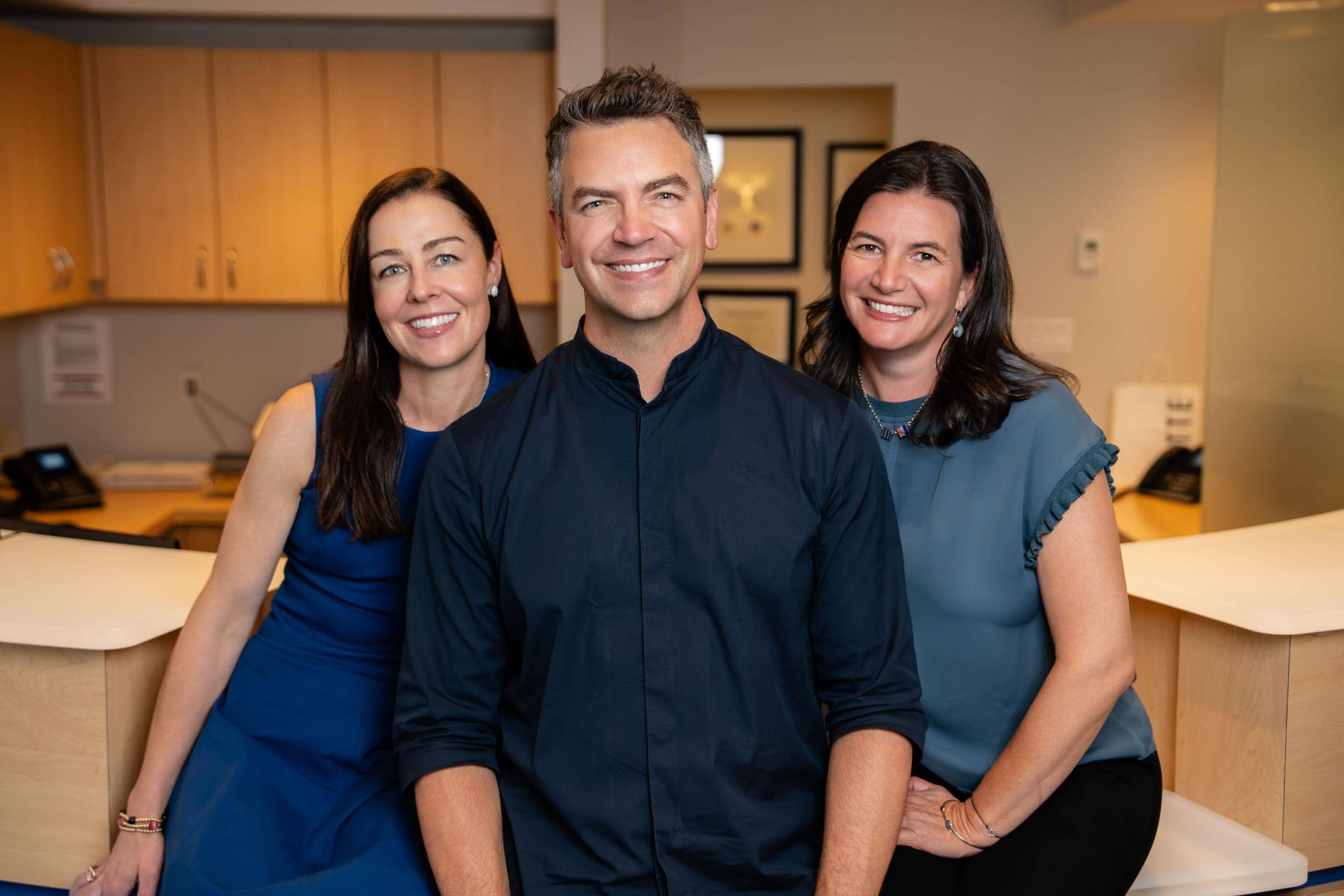 Three smiling professionals at Coppe & Sears Orthodontics, representing pediatric dentistry and orthodontic services, in a modern office setting.