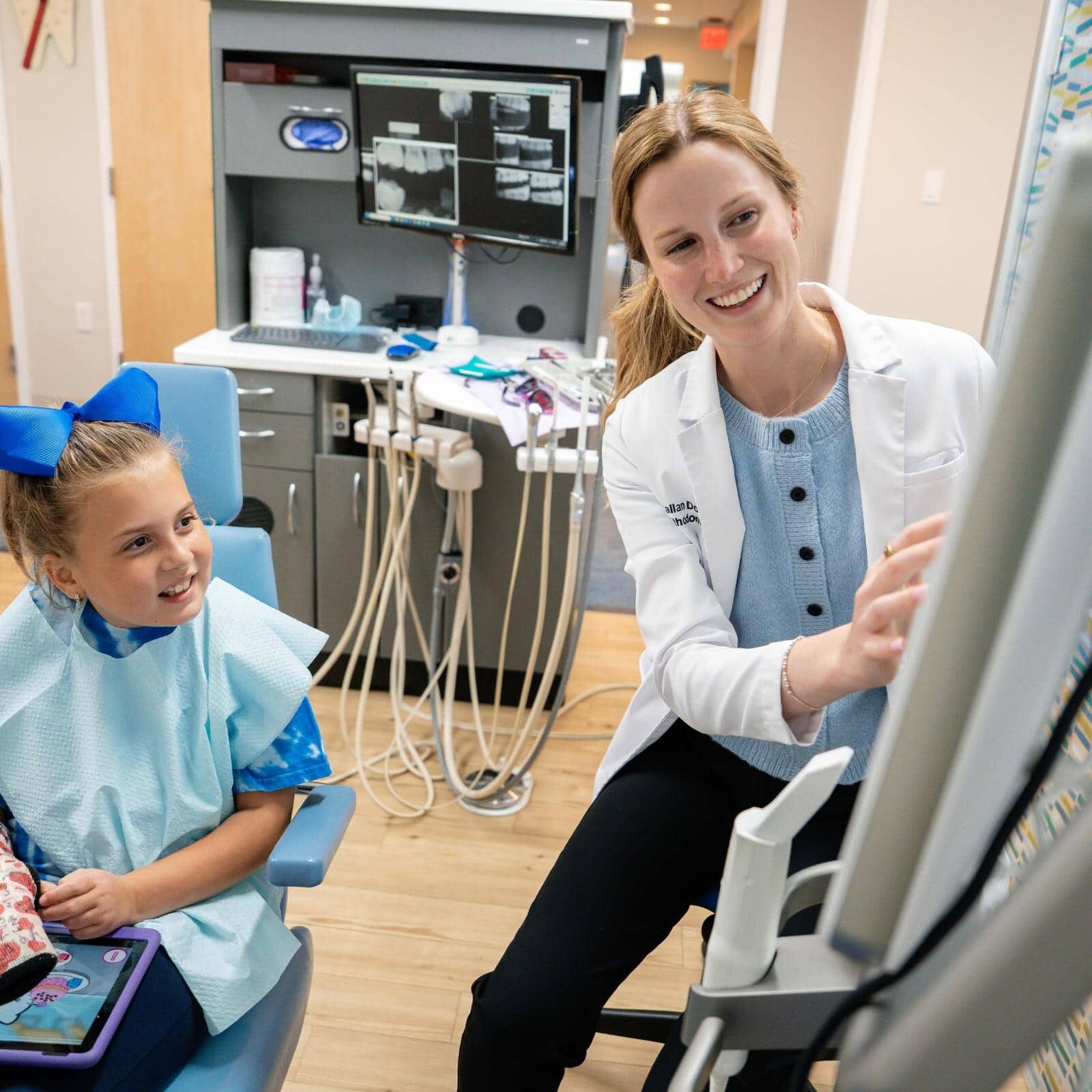 Child in dental chair smiling at pediatric dentist in modern office, showcasing Coppe + Sears Pediatric Dentistry and Orthodontics' friendly environment and care for kids in Lexington, MA.